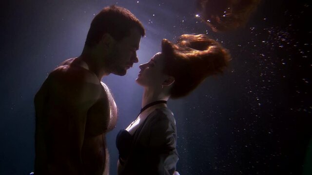 romantic underwater shot of loving couple in dark depth, unusual subaquatic date