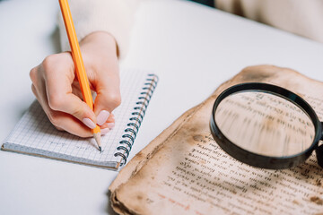 Researcher examines antique book with magnifying glass. Scientific translation of ancient...