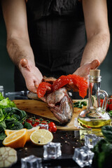 The big salmon is in the hands of the chef. He uses a knife to get the red caviar out of the fish.