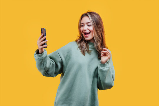 Attractive girl on a yellow background with a phone in her hands, she emotionally looks at the phone and smiles. Photo for advertising. Studio photo