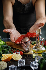 The big salmon is in the hands of the chef. He uses a knife to get the red caviar out of the fish.