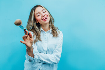 Girl makeup artist on a blue background, she is smiling and holding a makeup brush in his hand....