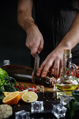 The big salmon is in the hands of the chef cook. He is using a knife to slice salmon fillet 