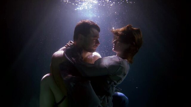 sexy man is hugging tenderly his young girlfriend underwater, loving pair is floating in depth