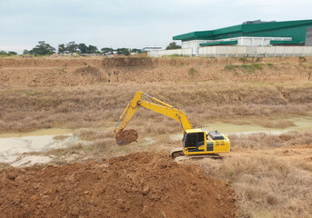 A yellow backhoe is loading the soil in a big pond.
