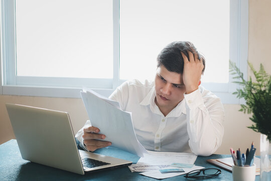 Young Asian Men Are Stressed Out In Business Office. Looking At Expense Bill And The Other Hand On Head, Thinking About Finding Money To Pay Credit Card Debt And All Bills. Concept Financial Problems.