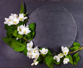 Empty shale round black serving board with white apple tree twig. Festive mockup for serving or recipes on spring holidays. Valentine's Day, Mother's Day, Birthday. Top view, copy space.