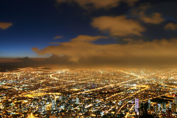Fototapeta premium Beautiful aerial view of Bogota city at night with business buildings, street lights, avenues and sky at dusk with clouds in the background. Selective focus. Concept of travel, tourism, vacation.