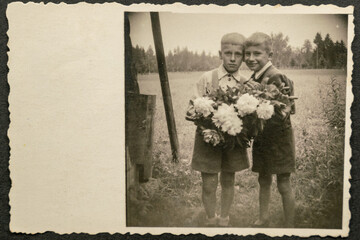 Germany - CIRCA 1930s: Two small kids standing and holding flowers in garden. Vintage archive Art Deco era photography