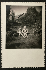 Germany - CIRCA 1930s: Group photo of two small kids sitting and holding cats in garden. Vintage archive Art Deco era photography