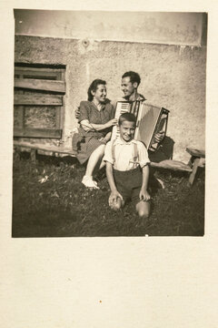 Latvia - CIRCA 1930s: A family shot of married couple with a child in porch outdoor. Man with accordions.Vintage art deco era photo