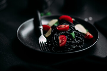 Black pasta with tomatoes and parmesan in a black plate