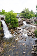 wide angle view of Almonte Falls, Ontario, Canada, a tiered and multiple segmented waterfall, surrounding small trees and grasses on bedrock during summer.