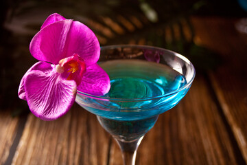 Summer tropical blue cocktail decorated purple orchid flower on the wooden background