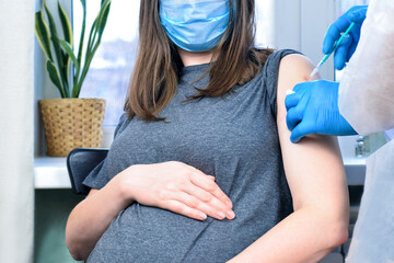 Doctor giving COVID -19 coronavirus vaccine injection to pregnant woman. Doctor Wearing Blue Gloves Vaccinating Young Pregnant Woman In Clinic. People vaccination concept.