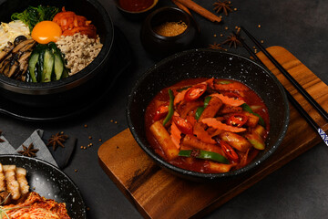 Korean Food Style : Top view of Hot and spicy Stir-fried rice cake ( Tteokbokki ) put in the black bowl or dish and placed on a wooden tray.