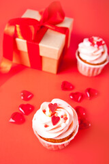 Valentines cupcakes cream cheese frosting decorated with heart candy and gift box on red background.
