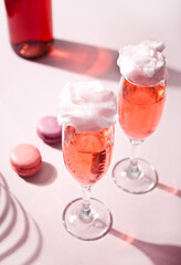 Glasses with sweet cotton candy pink cocktail and bottle on background