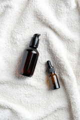 Amber glass bottles with essential oil and serum on white towel in bathroom. Natural organic SPA cosmetics. Flat lay, top view.