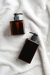 Amber glass dispenser bottles for shampoo or liquid soap on white towel. Natural organic SPA cosmetics. Flat lay, top view.
