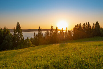 Fototapeta na wymiar Panoramic view of the Kama River from the hill, green meadow, rural road, sunset sky and sun rays.