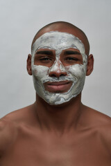 Close up portrait of cheerful young african american man winking at camera, using facial clay mask,...