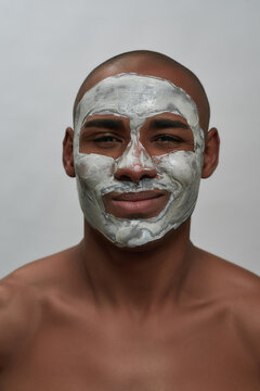 Close up portrait of cheerful young african american man winking at camera, using facial clay mask, posing isolated over gray background