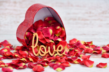 The word "Love" on a background of red rose petals falling out of a heart-shaped box - Powered by Adobe