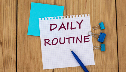 DAILY ROUTINE - word written in a notebook on a wooden background with a pen and clamps