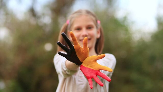 Happy outdoor portrait of child girl with hands painted in Belgium flag colors. Creative. Selective focus