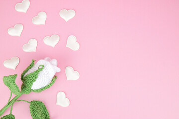 White knitted rose with white decorative hearts, laid out on a pink background on the right side of the image.