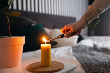 Girl lights Yellow candle made of bees wax with scent of honey on bedside table in bedroom Scandinavian interior - obrazy, fototapety, plakaty