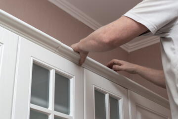 Furniture assembly. A man assembles a kitchen set, attaches stucco molding to the upper cabinets