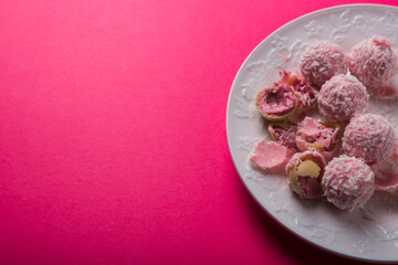delicious coconut candies with pink cream lie on a white plate on a bright pink background. Photos for printing, cooking courses. High quality photo