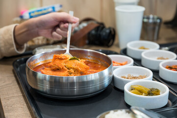 Hand using spoon scooping spicy kimchi soup and vegetable pickle on cup