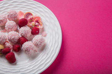 round white candy lie on a plate strewn with raspberries on a bright pink background. Photos for printing, cooking courses. High quality photo
