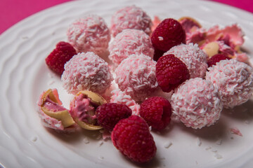 Delicious round sweets with coconut cream lie on a white plate strewn with raspberries. Photo of sweets. Photo of cooking. High quality photo