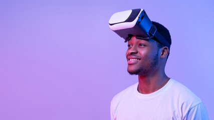 Fototapeta premium Smiling African American Guy Wearing VR Glasses And Looking Aside, Neon Light