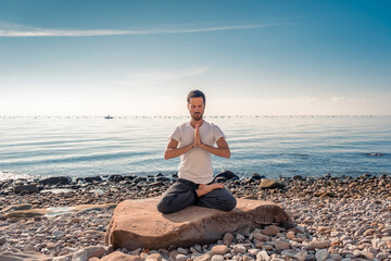Fototapeta na wymiar Attractive young man practicing yoga meditation and breathwork outdoors by the sea