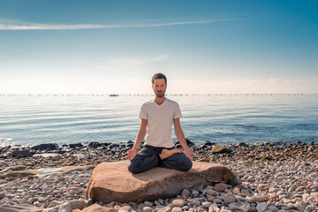 Naklejka na ściany i meble Attractive young man practicing yoga meditation and breathwork outdoors by the sea