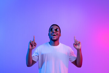Excited Black Guy Standing Under Neon Light Pointing Fingers Up Above Head