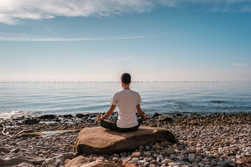 Attractive young man practicing yoga meditation and breathwork outdoors by the sea
