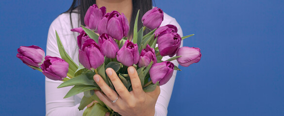 Mano sosteniendo un ramo de tulipanes morados y mostrando un anillo de compromiso.
