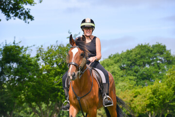 Happy smiling woman enjoys riding her bay horse in the English countryside on a sunny summers day.