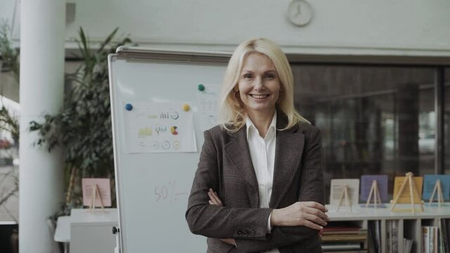 Self-assured friendly attractive middle-aged businesswoman in a stylish jacket standing with folded arms smiling at the camera