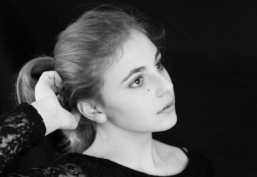 Beautiful blond girl on a black background (Studio lighting). Black and white portrait. She has a pony tail, posing and looking to the side.