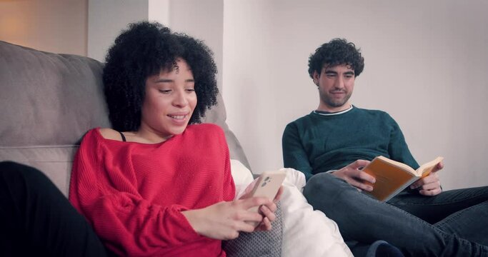 Couple at home reading a book and entertaining themselves with cell phone