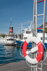 Obraz premium lifebelt on a pier with boats and ferries in the background