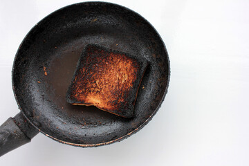 Piece of burnt toast bread on a frying pan on a white background. Top view, copy space 