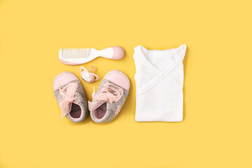 Baby rompers, shoes, pacifier and hair comb on yellow background
